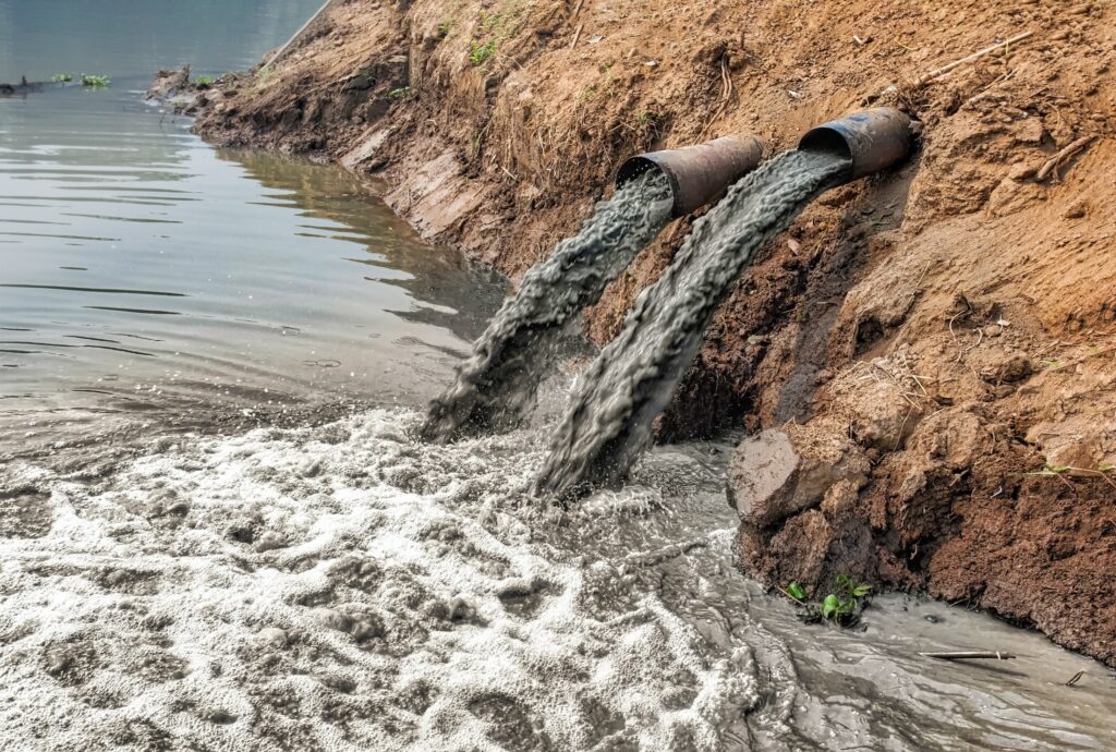 Pipes dumping pollution in a river | Adobe